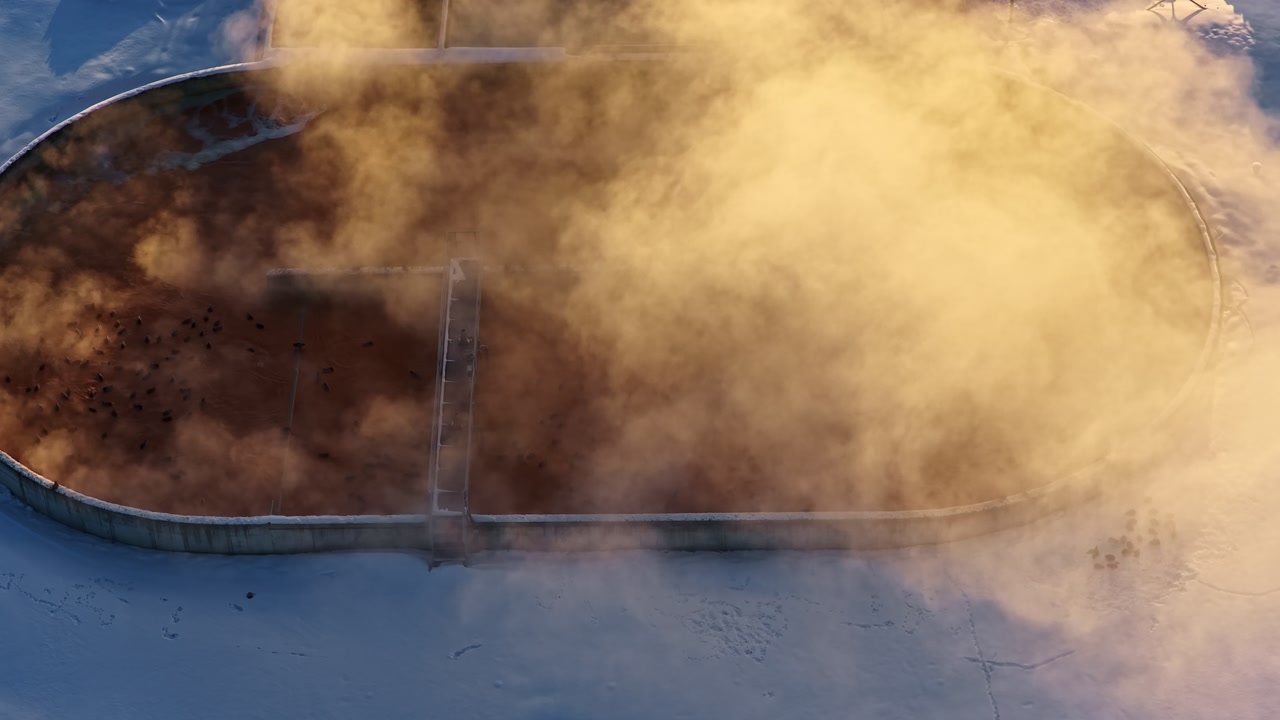 Aerial close-up of a steaming clarifier basin in winter, with golden vapor over a snow-covered treatment plant, showing municipal water infrastructure in freezing conditions.