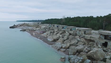 vista aérea de los edificios abandonados de la fortificación junto al mar en los fuertes del norte de karosta en la playa del mar báltico, día nublado, amplio tiro ascendente de drones avanzando