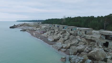 aerial view of abandoned seaside fortification buildings at karosta northern forts on the beach of baltic sea , overcast day, wide ascending drone shot moving forward