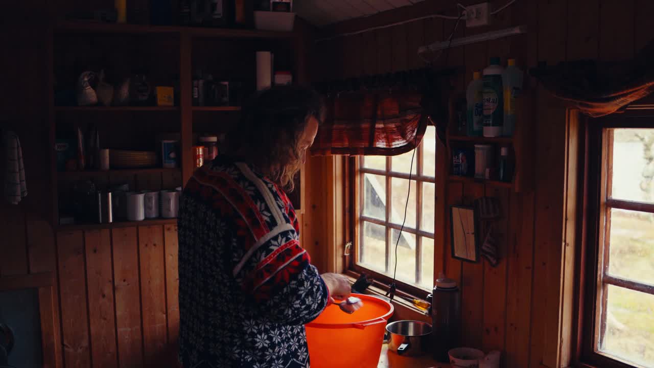 Caucasian Man Cleaning Spoon Using Brush In A Small Pail In The Kitchen. Close-up Shot