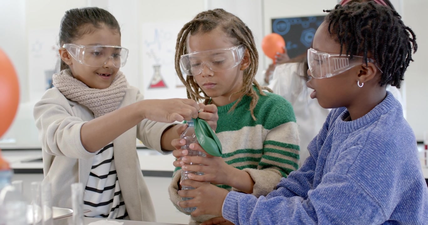 African American preteens securing green balloon onto bottle, watching foam gas inflating it in lab