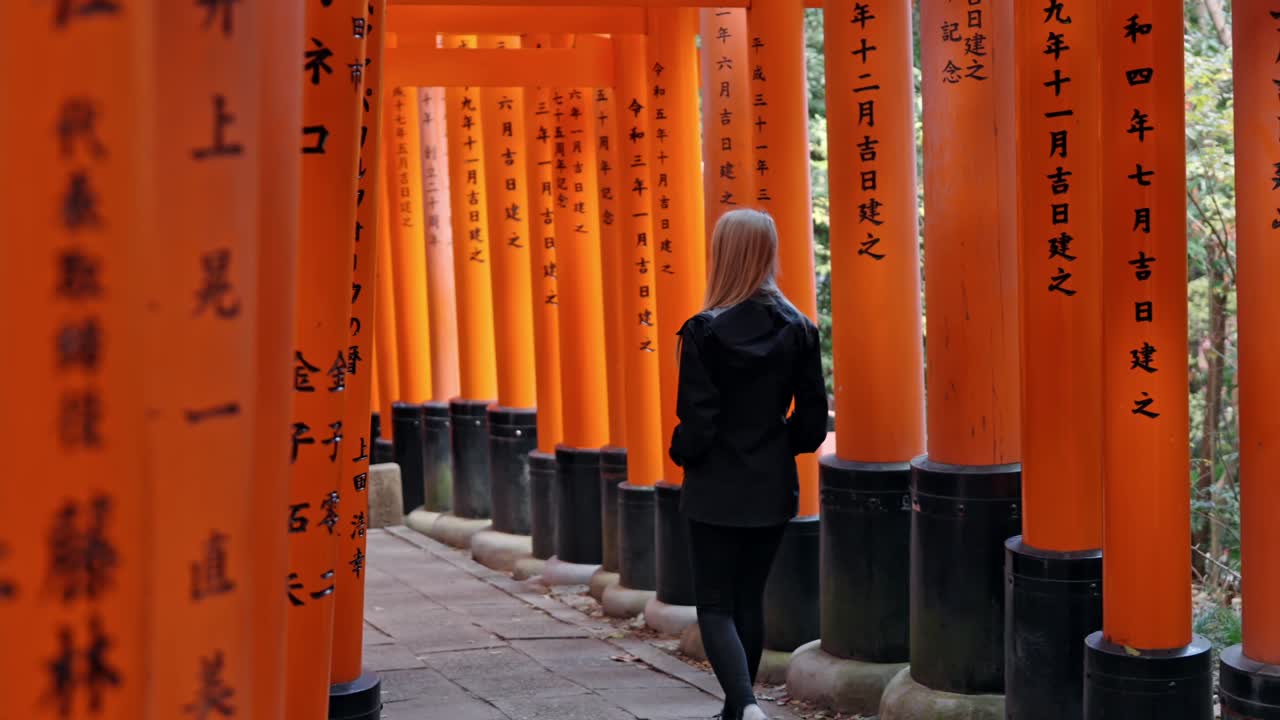 A woman strolls through the iconic torii gates of Fushimi Inari Shrine in Kyoto, Japan.