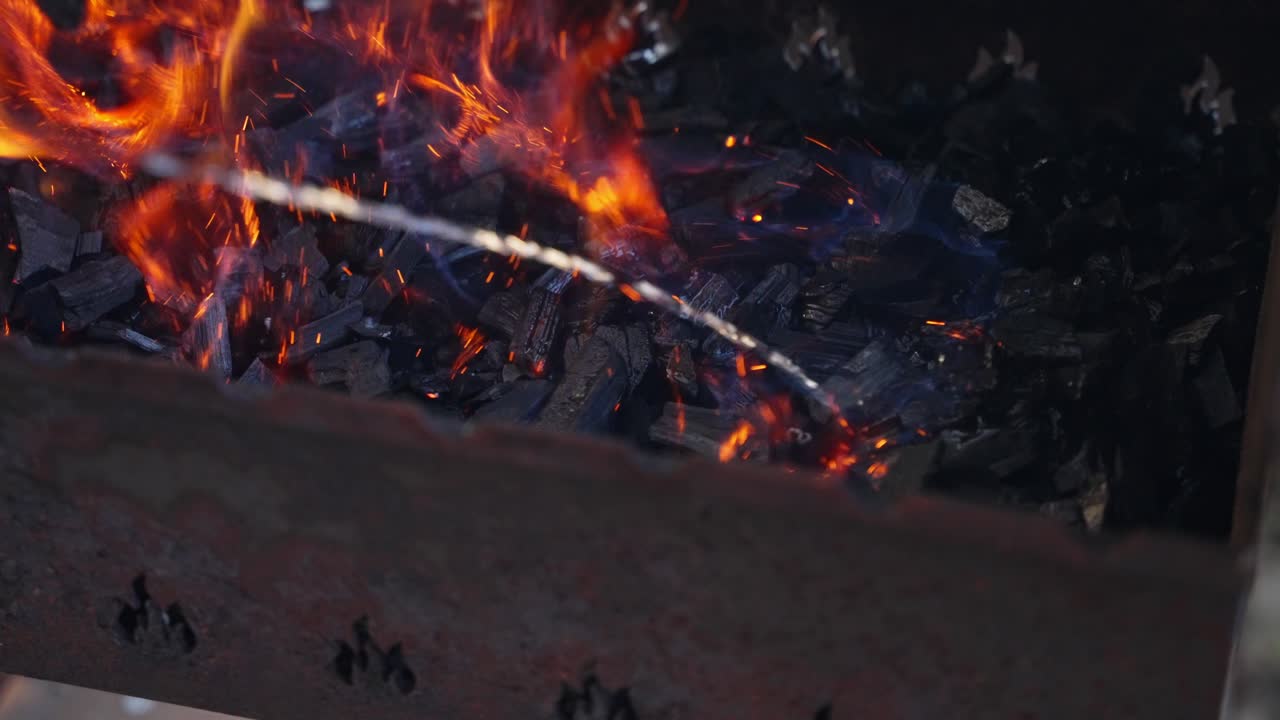 Bright flames rising over charcoal spraying with gasoline lighter fluid in a metal grill, slow motion