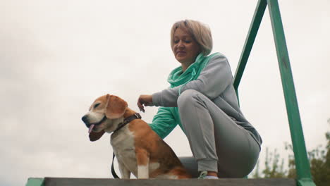 canine specialist rubbing ears and body of seated dog smiling warmly showing affection trust and deep bond outdoors under cloudy sky creating emotional connection and happiness