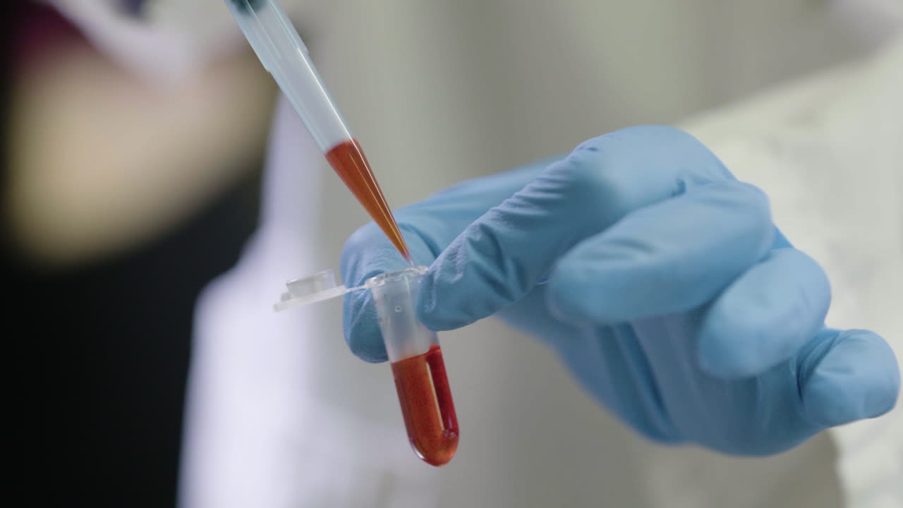 A liquid is transferred from a test tube to a pipette and back again by gloved hands.