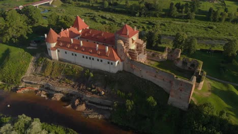 drone panorama of bauska castle in latvia, with scaffolding and ruins next to the restored castle