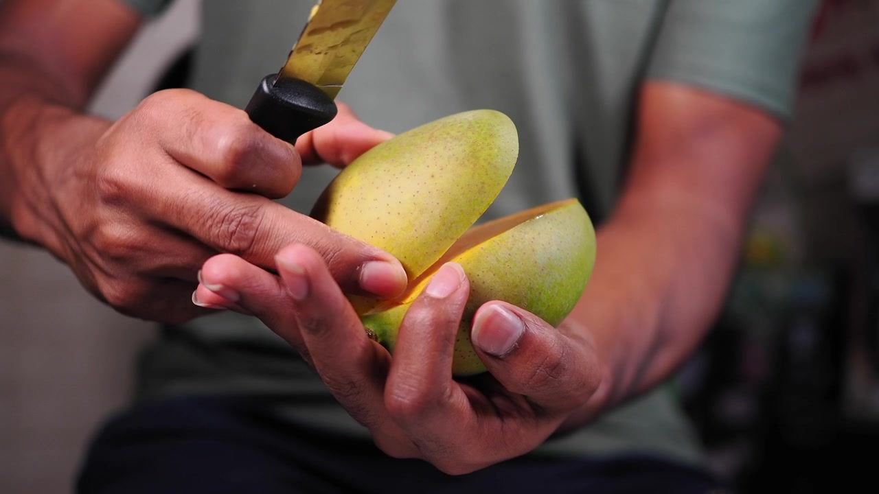 Person som skjærer en fersk mango med en kjøkkenkniv