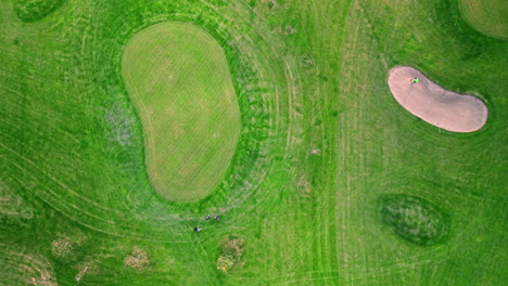 disparo superior de un golfista en la trampa de arena, haciendo un par de movimientos de práctica, luego disparando hacia el verde, y finalmente rastrillando el bunker de la trampa de arena para limpiar antes de irse