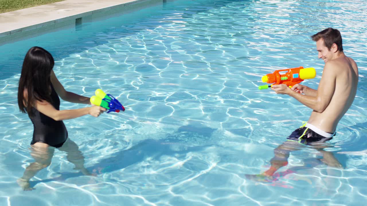 Coppia felice che gioca con pistole ad acqua in piscina