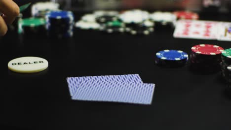 a hand hands out playing cards on black table with dealer chip on the side and poker chips