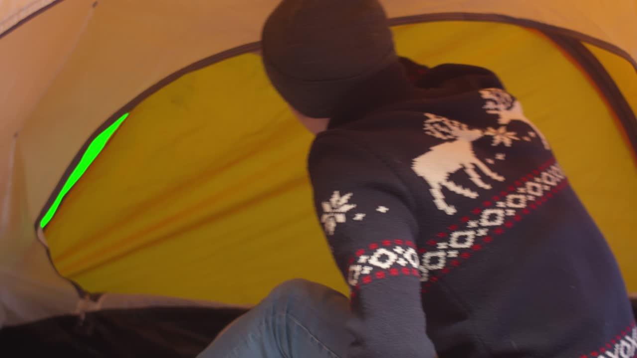 스웨터를 입은 남자가 텐트 안쪽을 열고 텐트 안에 있는 남자가 입구를 열고 풍경을 바라보고 있다.