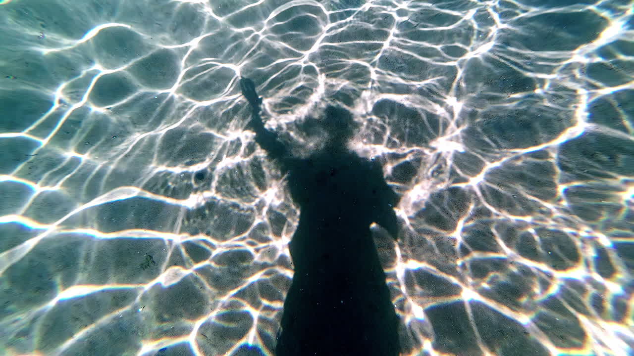 Artistic underwater shot of a swimming person's silhouette on the ocean floor