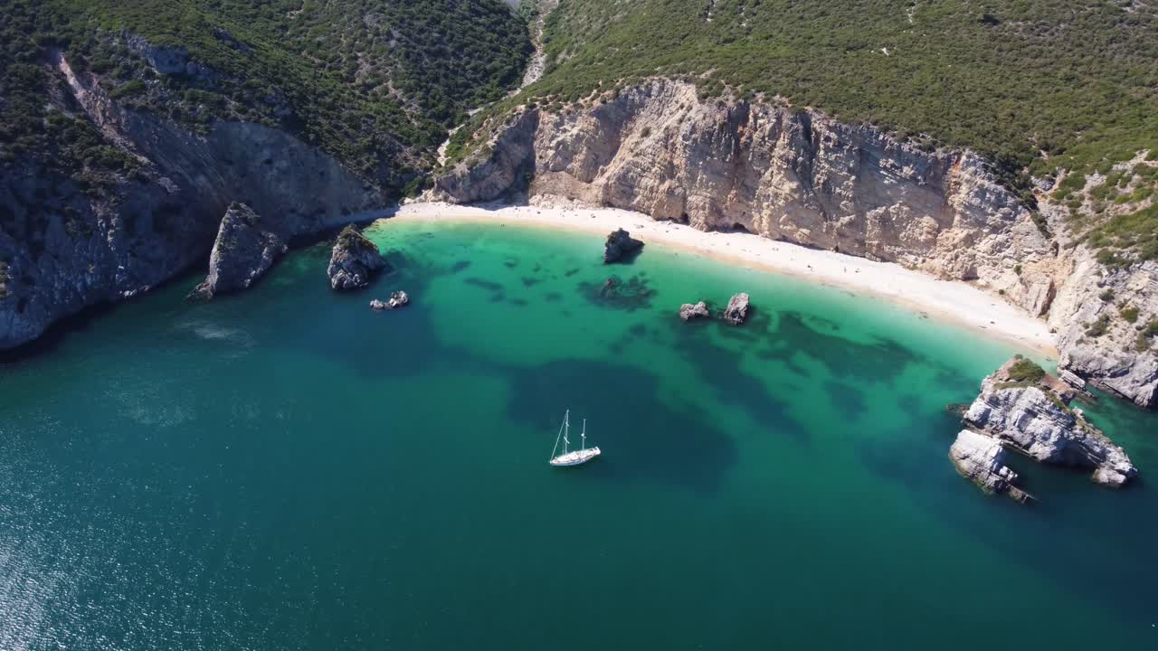 Ripresa aerea ascendente in allontanamento di uno yacht che ormeggia presso una spiaggia dall'aspetto tropicale in Portogallo