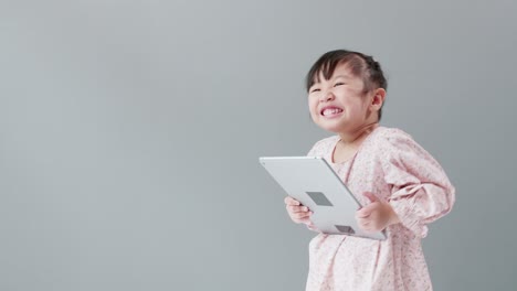 카메라를 보고, 태블릿을 보고 스튜디오에서 웃고 있는 작은 아시아 소녀