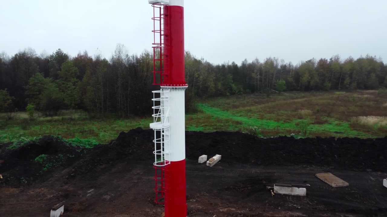 Letecký pohled na červenobílý průmyslový komín na staveništi.