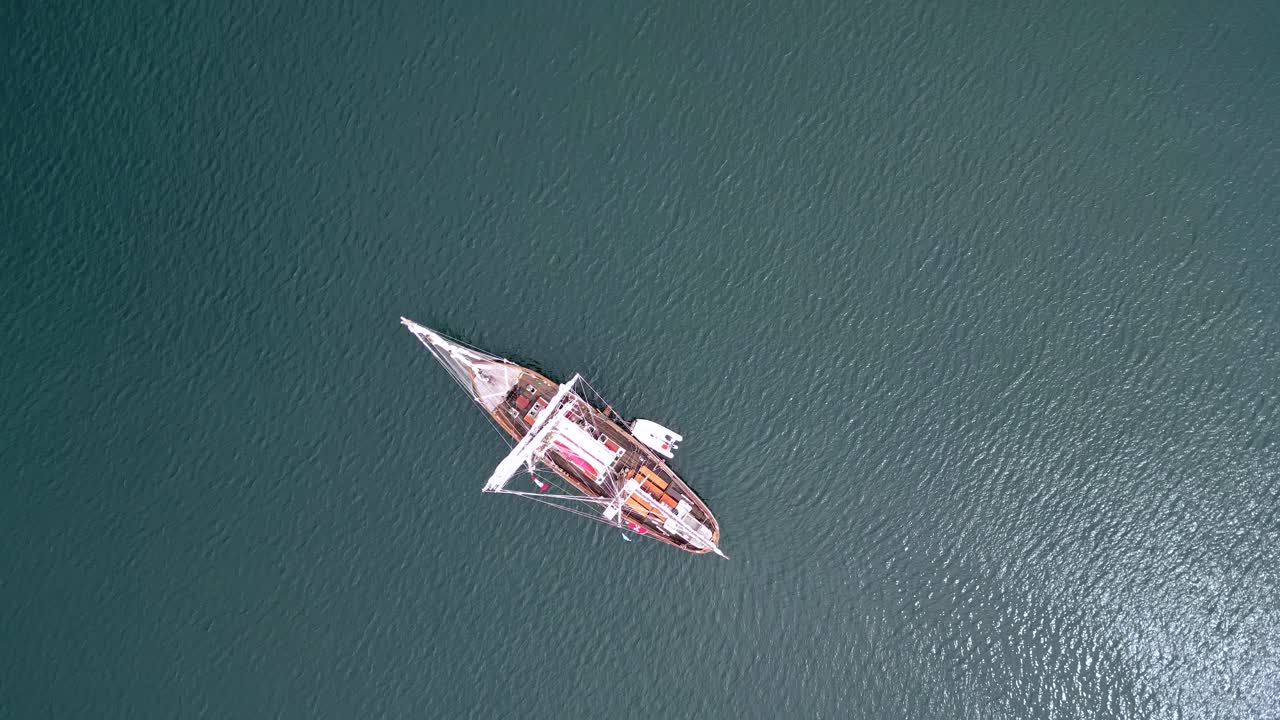 Top down aerial view of sailing yacht on turquoise ocean water near Isle of Mull. Bird's eye perspective of sailboat cruising through calm Scottish waters. Beautiful maritime scene in Scottish Hebride
