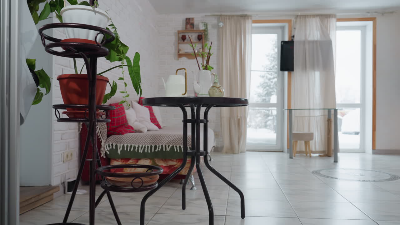 Cozy modern room decorated with green plants, chair, television, flowing curtain and natural light reflecting on tiled floor and brick wall, creating bright airy ambience ideal for indoor greenery