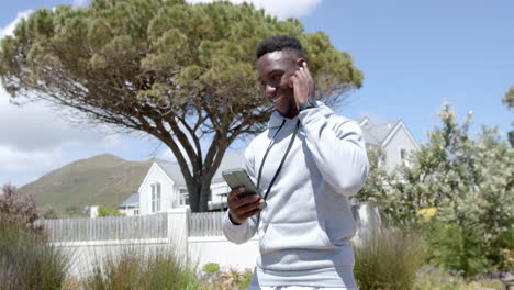 Happy-african-american-man-jogging-and-using-headphones-and-smartphone-on-sunny-day,-slow-motion