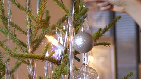 woman hand hanging silver christmas baubles in real christmas tree, close up