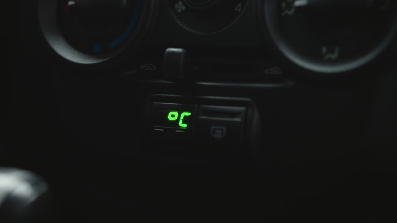 Close up of car dashboard climate control digital temperature display showing 3.9 degrees with dials and buttons in blurred background highlighting green LED readout and cabin environment details