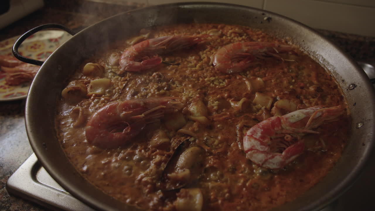 Paella de frutos do mar valenciana tradicional cozinhando lentamente em uma panela com camarões, lulas, mexilhões, vapor e bolhas fervendo