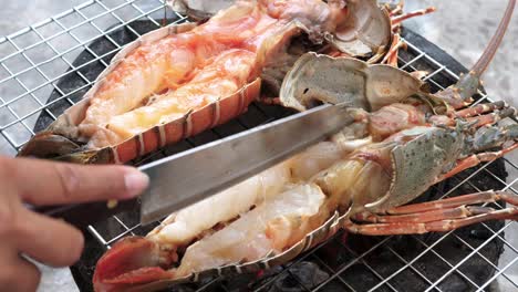 delicious grilled half lobster tail on the grill grid, chef using knife- close up
