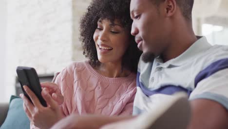 happy african american couple using smartphone together in living room