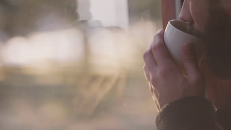 bearded hipster traveler holding coffee mug in wooden cabin