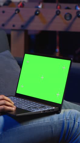 vertical video african american young guy using device with green screen from his sofa