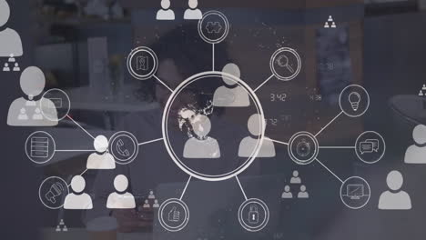 animación de un globo giratorio e iconos digitales flotando sobre un hombre biracial que usa un teléfono inteligente en la oficina
