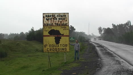 a man stands next to a sign announcing the equator crossing