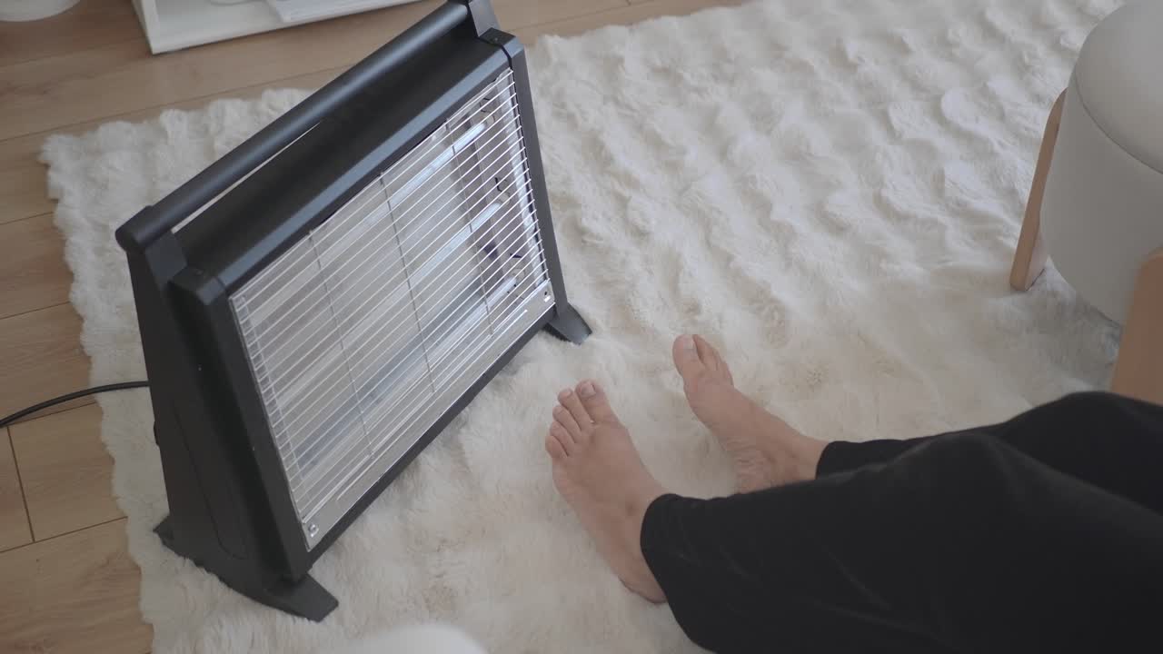 Person Warming Bare Feet with Electric Heater on a Cozy Rug