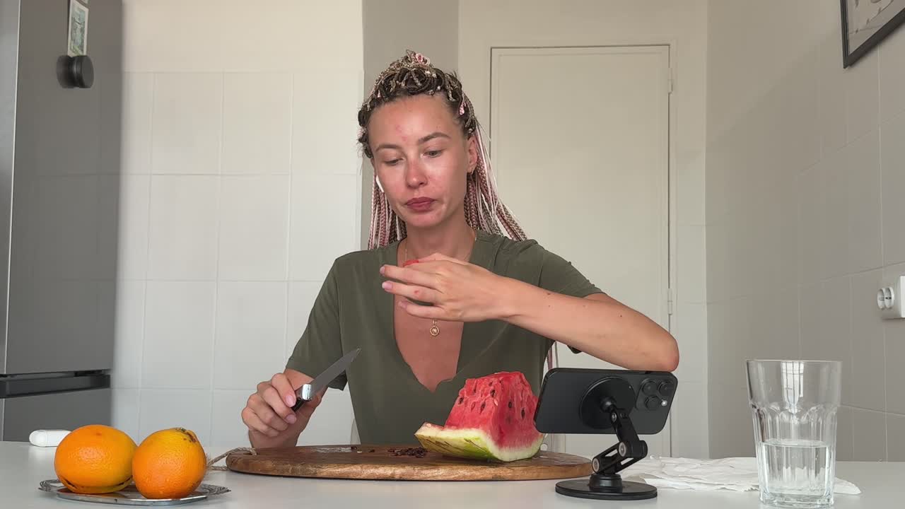 Mladá žena krájí a jí meloun v kuchyni.