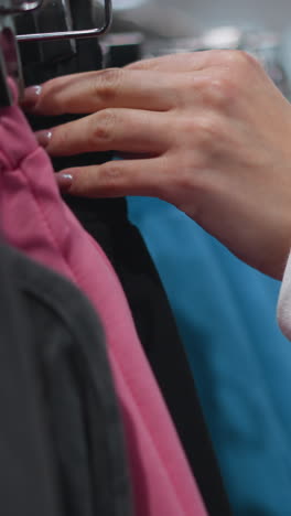 mujer joven navegando por el estante de ropa vibrante en la tienda minorista, inspeccionando suavemente las prendas de vestir coloridas con precisión y atención a los detalles, entorno bien iluminado