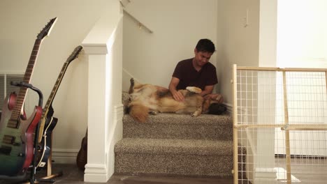 man petting his dog while sitting on the stairs inside the house