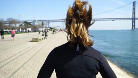 Back view of sporty young woman running along embankment
