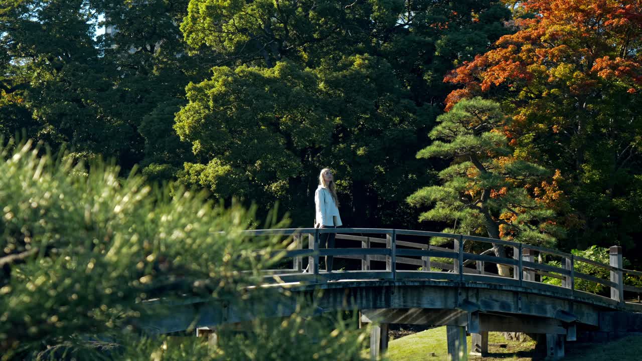 Girl walking across a traditional wooden bridge in Hamarikyu Gardens, Tokyo, surrounded by the vibrant colors of autumn.