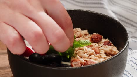 preparing a yogurt parfait with granola, berries, and mint