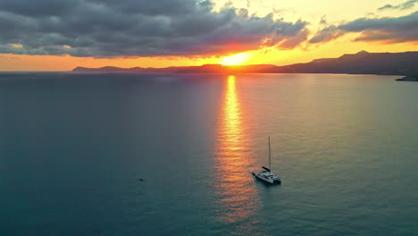 aerial view circling a catamaran sailing the coast of crete, sunset in greece