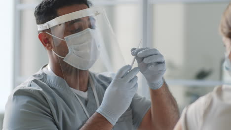 Médico-Con-Uniforme-Protector-Vacunando-A-Una-Paciente