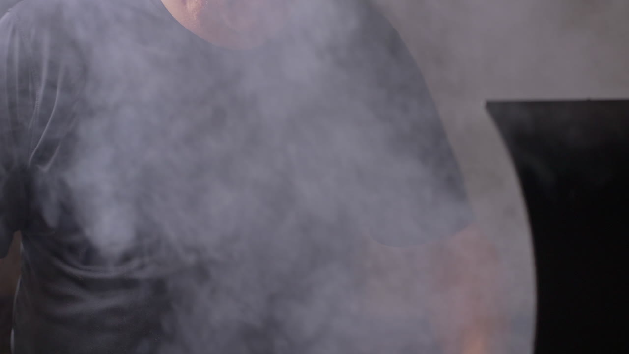 Tilt down from man to opening BBQ pit lid and grabbing tongs