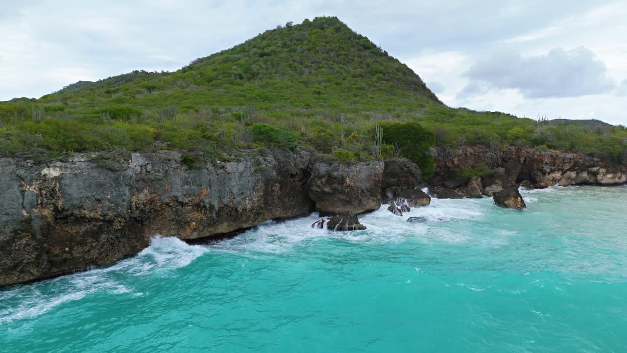 Acqua dell'oceano verde schiuma marina si infrange contro scogliere rocciose e grotte su un'isola caraibica