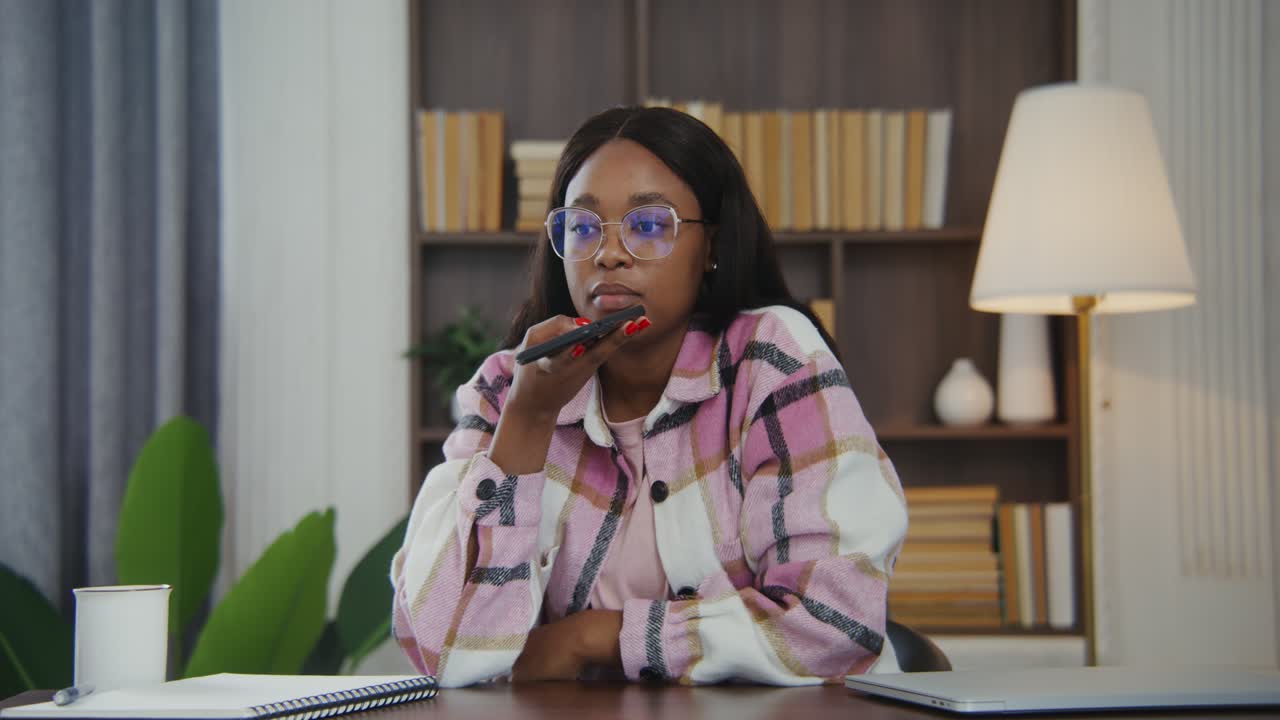 mujer en la oficina de su casa usando el micrófono de su teléfono inteligente