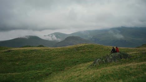 Two hiker friends sit on a rock and watch the clouds blow over the mountains