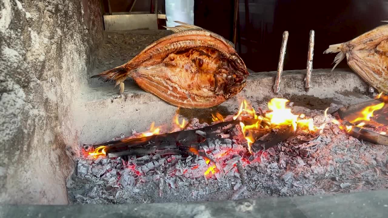 Bream fish at an Iraqi restaurant butterflied, smoked, skewered, and grilling over a fire pit in slow motion
