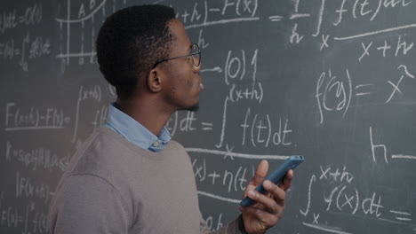 student using smartphone in a classroom with math equations on chalkboard