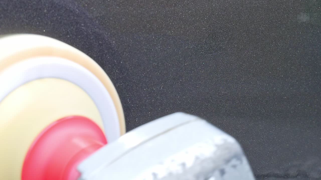 Extreme close up machine polishing grey paint with rotary machine polisher and an orange hex polishing pad