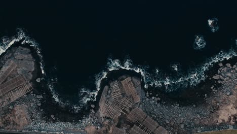 lofoten islands, nordland, norway - rugged arctic coastline meets tradition, where ocean waves crash beside historic fish drying racks - aerial ascend shot