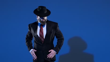 a mysterious man in a black suit and fedora posing on a blue background