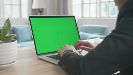 un hombre de negocios asiático con traje de negocios escribiendo en una computadora de pantalla verde mientras trabaja en casa.